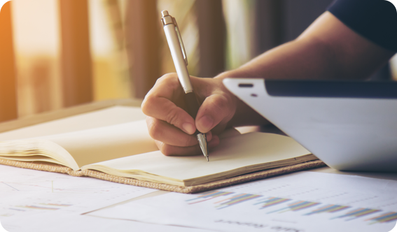 right hand writing in book with papers on a table